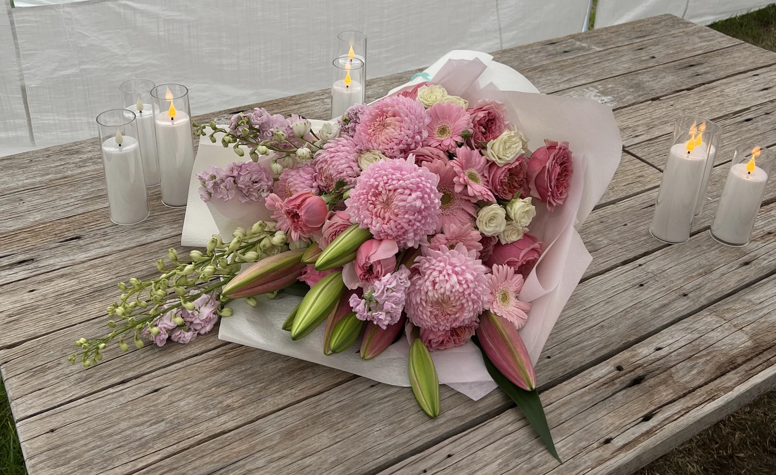 A soft pink Chirri Floral bouquet styled on a wooden table with candles.